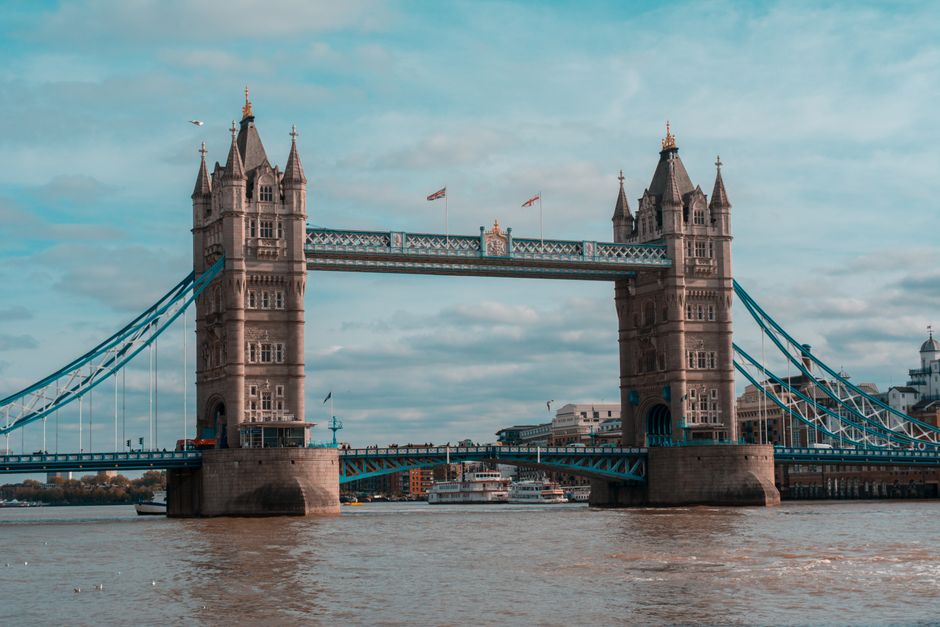 A black-and-white photograph taken from a low angle on the Tower Bridge Road, showing the Tower Bridge's central tower with its detailed gothic architecture and arched opening at the base. The image c